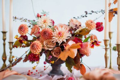 Beautiful flower composition with autumn orange and red flowers and berries. Autumn bouquet in vintage vase on a wooden table with pink tissue and candles