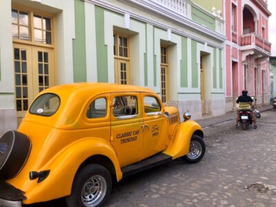 Žuti oldtajmer sa natpisom Classic Car Trinidad parkiran uz pastelnu zgradu