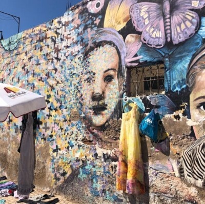 Ulični mural sa licima i leptirima i odeća izložena na prodaju ispred njega