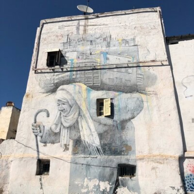 Mural starice sa štapom naslikan na beloj fasadi visoke zgrade