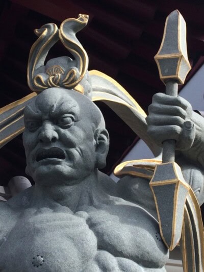 Kamena statua ljutitog čuvara hrama sa pozlaćenim ukrasima drži koplje u ruci