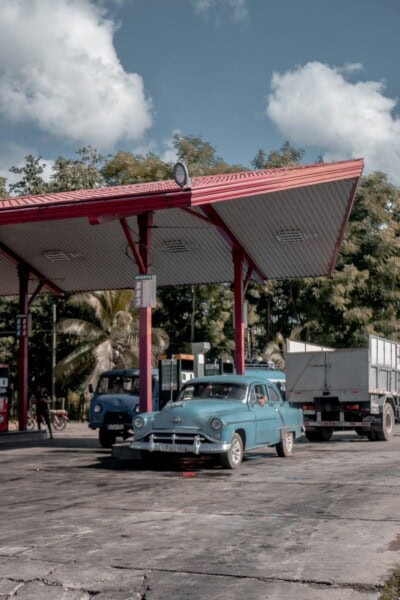 Stari plavi automobil i kamion na benzinskoj pumpi sa crvenim krovom