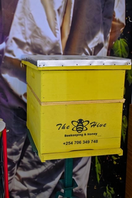 Yellow beekeeping hive box labeled The Hive on a green stand.