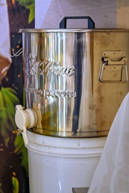 Large stainless-steel honey container with a spigot and handle.