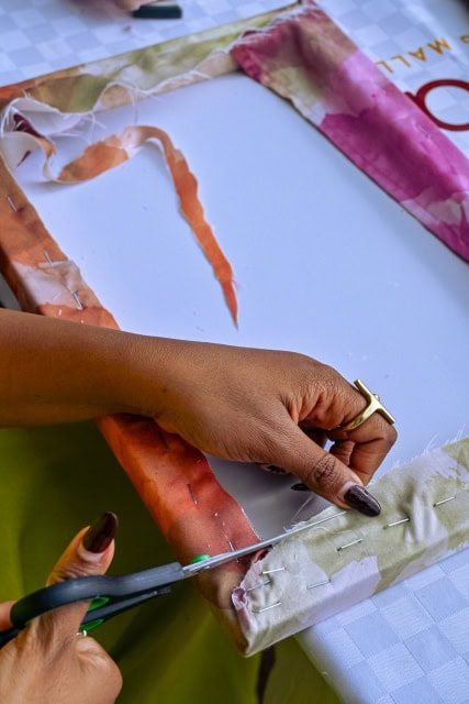 Close-up of a participant trimming and pinning fabric around a frame at the Galleria workshop.