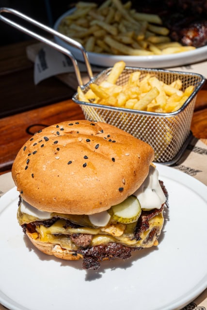 Loaded burger served with fries in a wire basket on a white plate.