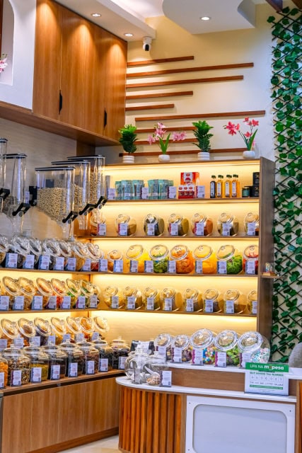 Interior display with illuminated shelves, nut dispensers, packaged products, and decorative plants