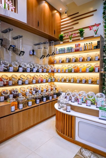 Bright retail interior with illuminated wooden shelves filled with jars and packaged bulk foods beside a curved display counter.