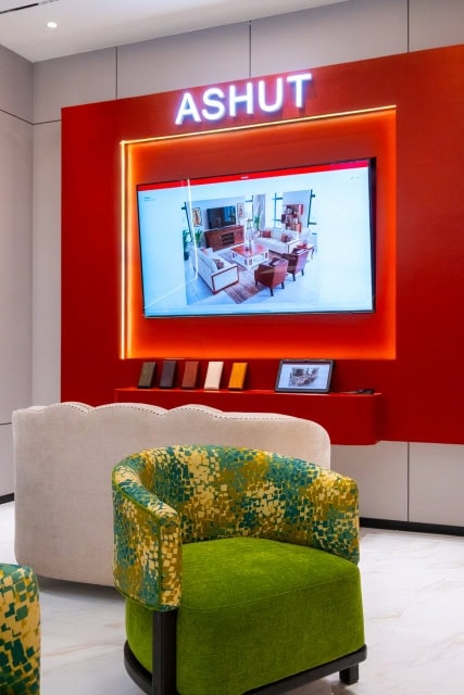 Showroom interior with ASHUT signage, a wall-mounted screen and a green patterned armchair.