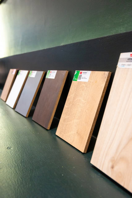 Labelled wood and laminate finish boards displayed on a dark green wall