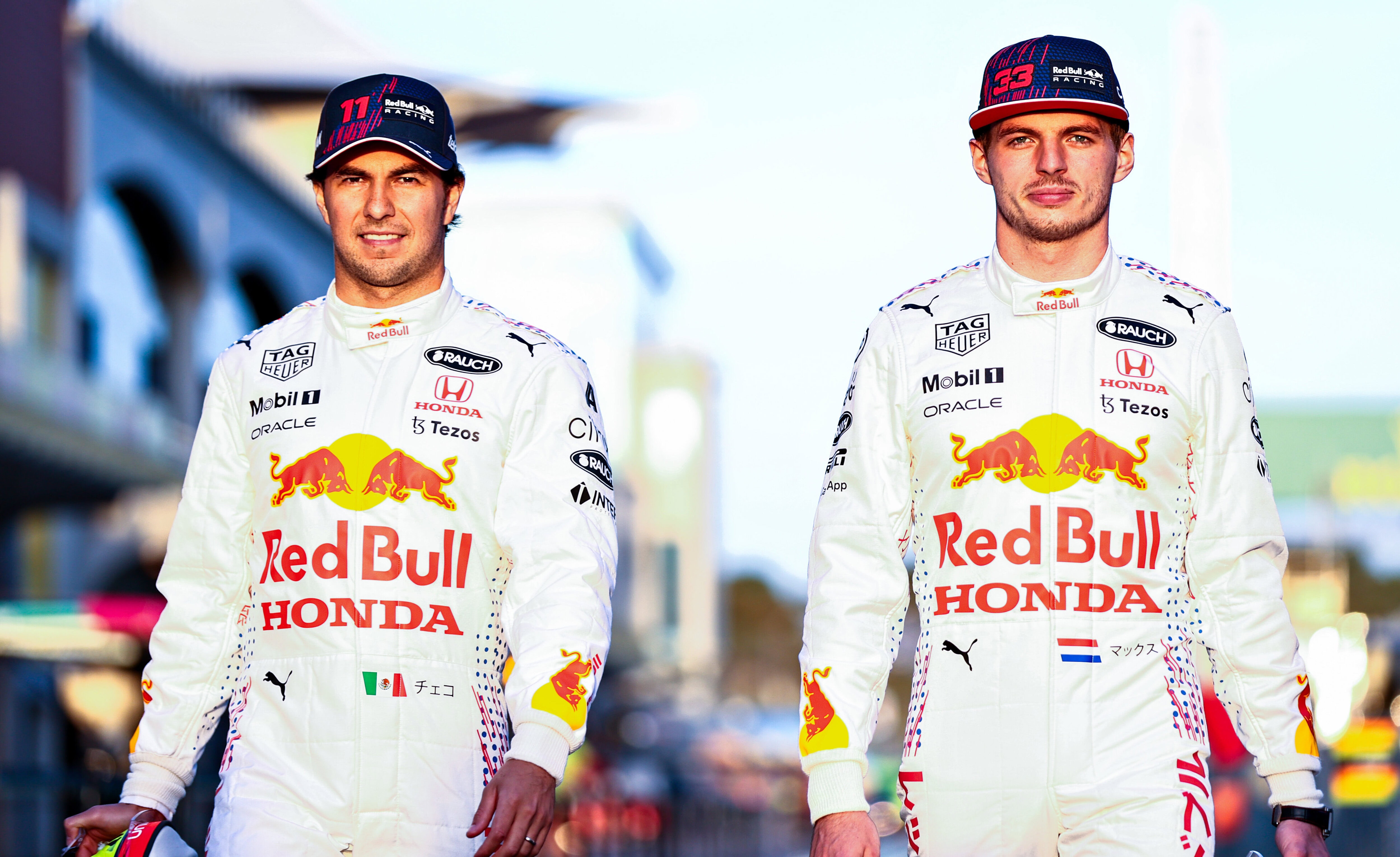 Formula 1 drivers Max Verstappen and Sergio Perez walking on a race track wearing white Red Bull jumpsuits