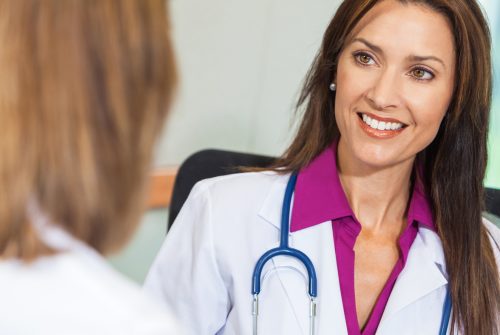 Woman Doctor in Hospital Meeting with Female Colleague Happy, smiling, woman doctor in white lab coat with stethoscope in hospital office meeting with female colleague