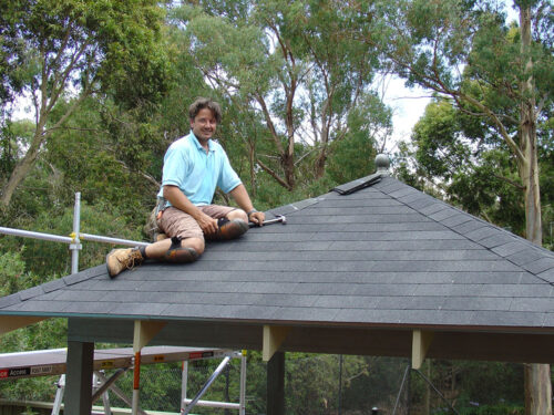Homeowner installing DIY roof shingles with ladder Australia