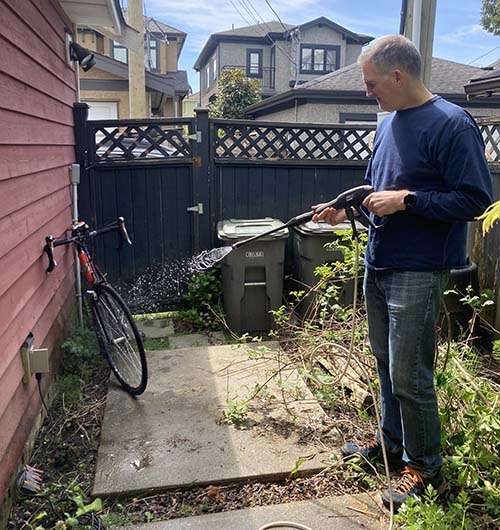Man washing bike with a pressure washer from a distance