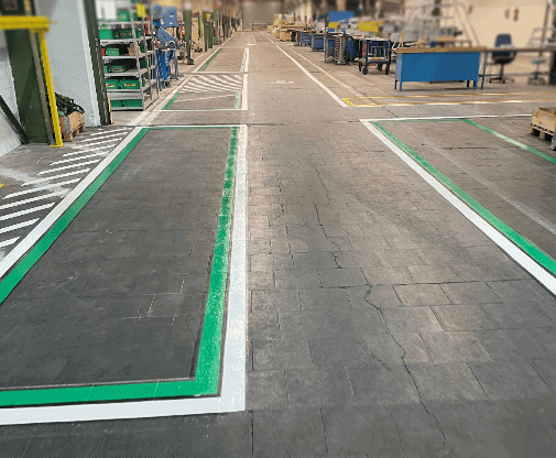 Bodenmarkierung eines Fußgängerwegs in RAL 9016 Verkehrsweiß in einer Halle, ergänzt durch Stellplätze in RAL 6024 Verkehrsgrün. Diese Markierungen sorgen für eine klare Trennung von Geh- und Stellbereichen und erhöhen die Sicherheit und Organisation im Raum