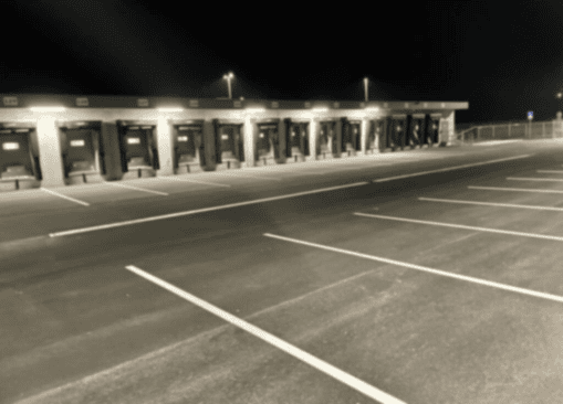 Laderampen und Verkehrsflächen vor einem Logistikzentrum bei Nacht, erstellt von einer spezialisierten Bodenmarkierungsfirma das Bild ist verschwommen.
