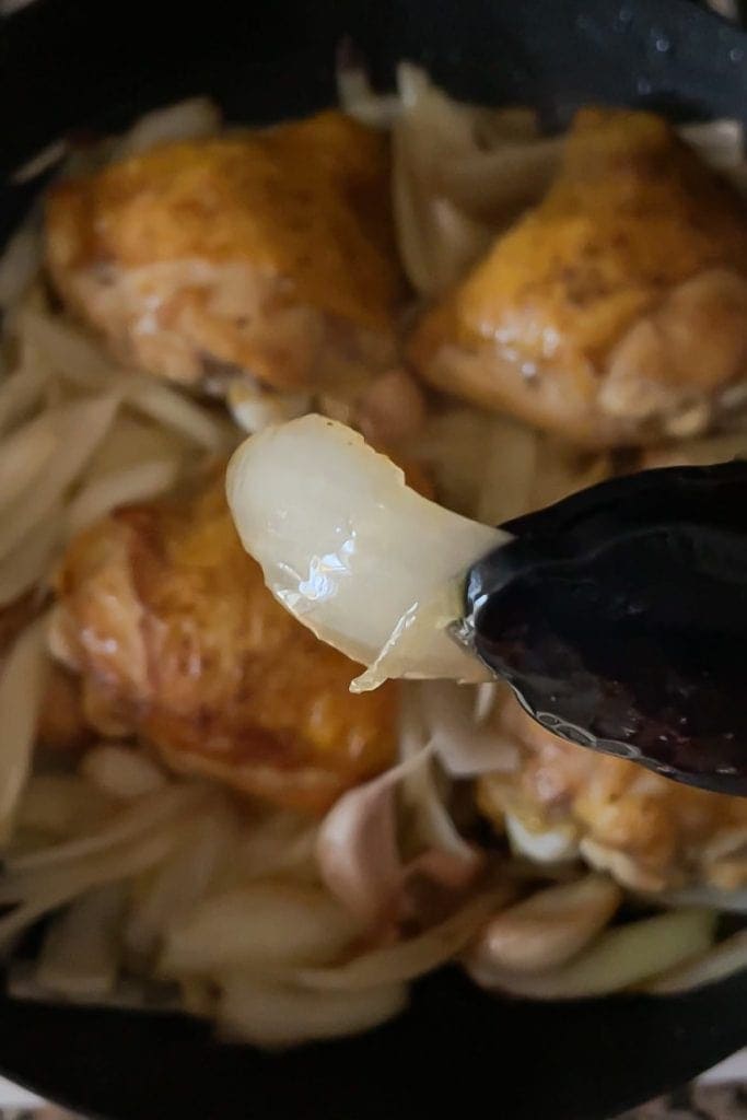 Cava braised chicken. Translucent onion held by a pair of tongs to show how the onion should look like right before adding the cava to the pan.