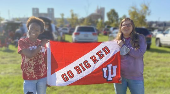 Two students smiling holding a "go big red' Banner