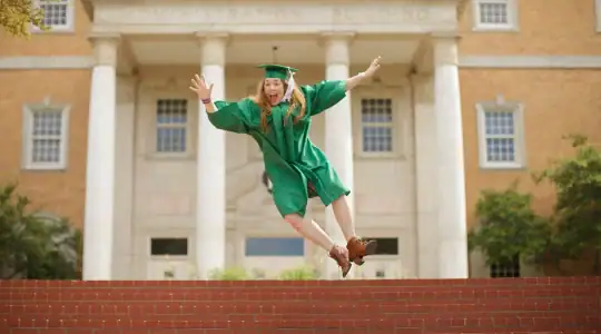 College Student with graduation gown jumping for joy