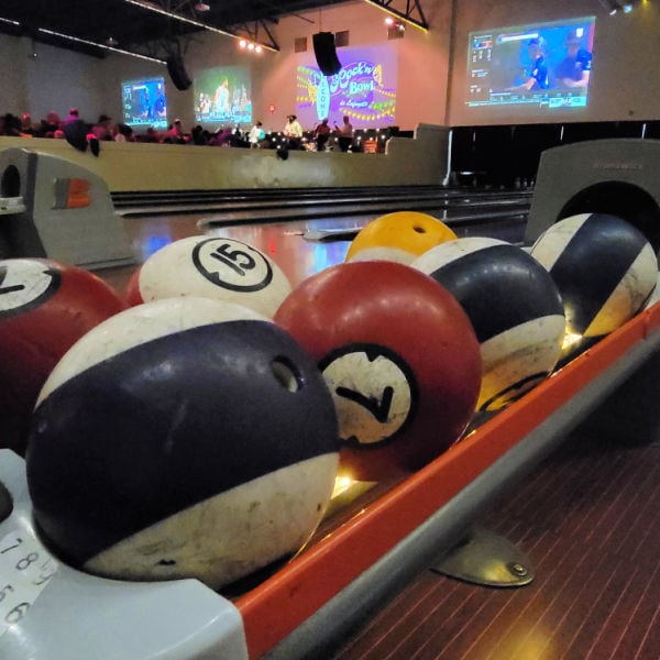 close up of bowling balls decorated to look like billardballs in bowling rack with big screens in background