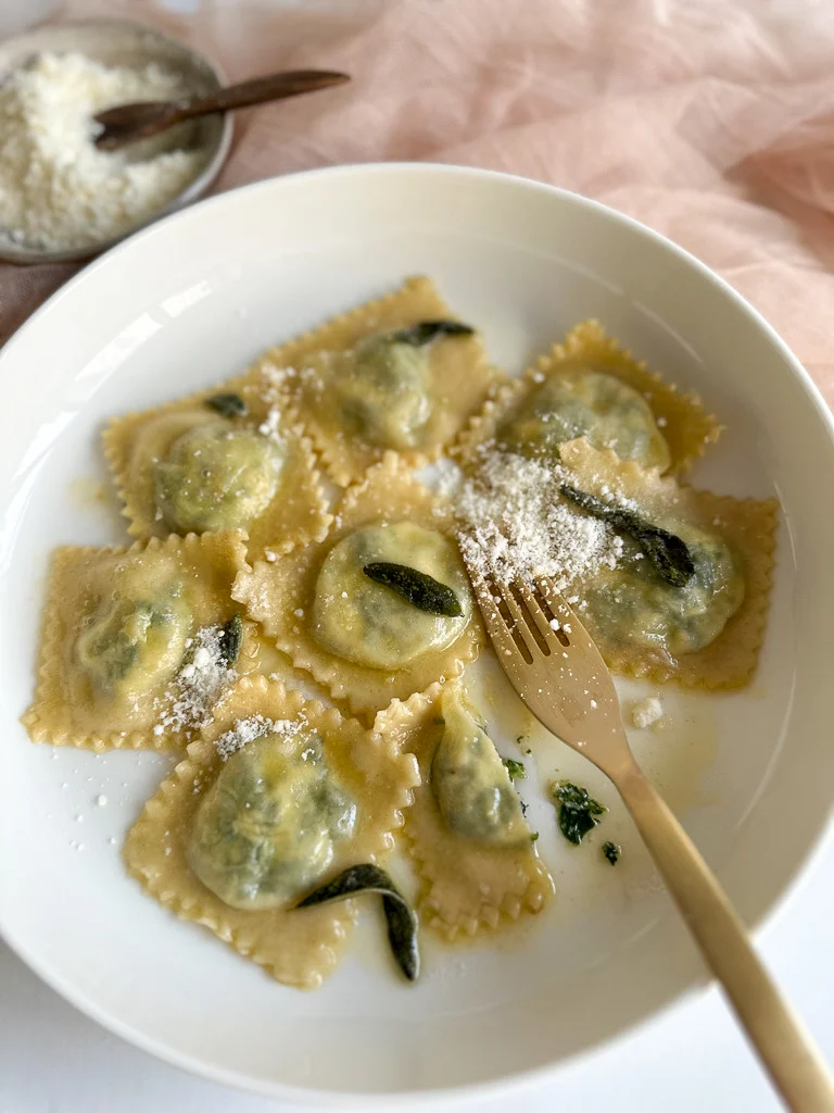 Homemade Ravioli with spinach and ricotta in a plate with sage and a gold knife