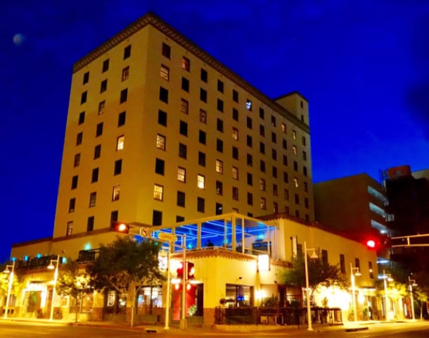 Heavy late-1930s building rises up to night sky. Ground floor is lit with colorful lights at theis cool places to stay in Albuquerque
