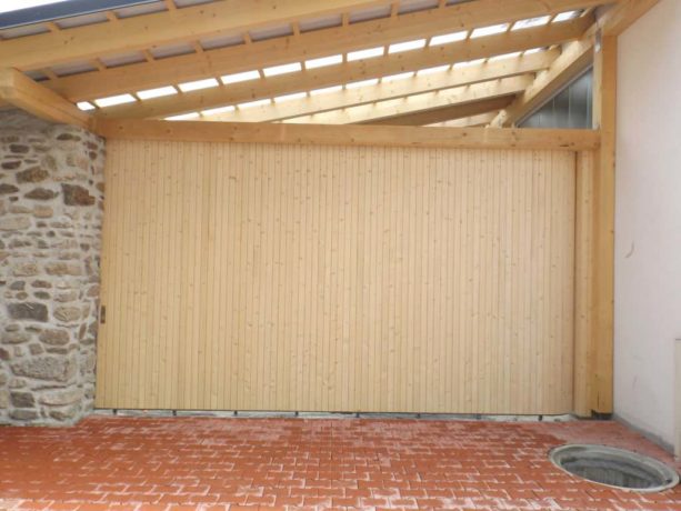 the combination of natural stacked stone wall, brick paver, and a contemporary side sliding garage door