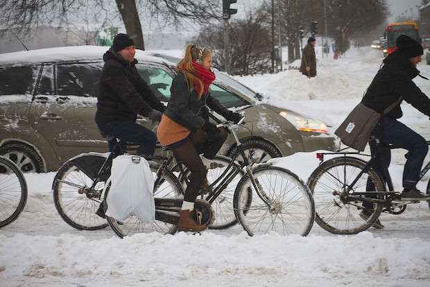 Three people riding bikes in the snow with toques and earmuffs
