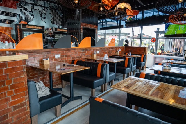 Restaurant interior with wooden tables, black and orange booth seating, brick walls and hanging lights.