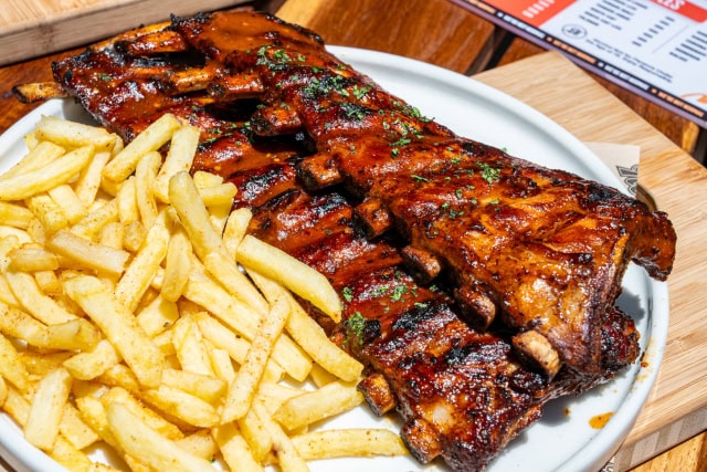 Full rack of glazed barbecue ribs served with fries on a white plate.