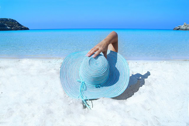 Blue sky, Blue waters, white sand. A person lying in the sand hidden by a blue, beach hat to enjoy and protect from the sun.