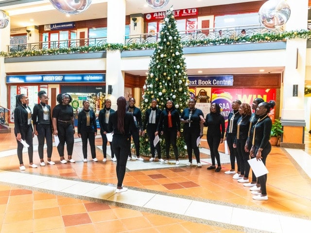 Group of singers in black outfits stand around a decorated Christmas tree in a mall atrium