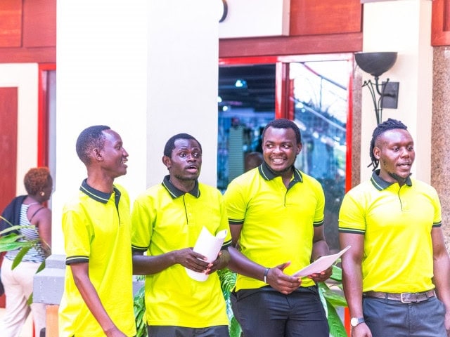 Four men in bright yellow polo shirts holding papers and standing together indoors