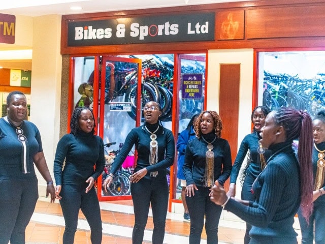 Women in black outfits sing together outside a bicycle shop