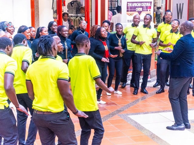 A large group of choir members gathered indoors, with several singers in matching bright yellow shirts