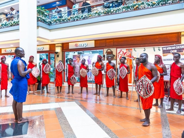 Cultural performers in red clothing hold decorated shields during a mall performance