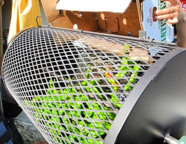 roller cage filled with green chiles and more from a produce carton labeled Melissa's Produce being dumped inside. shows How to Roast Green Chiles