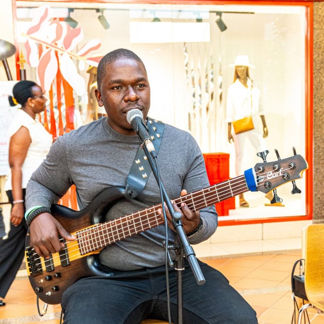 Musician singing into a microphone while playing a black bass guitar