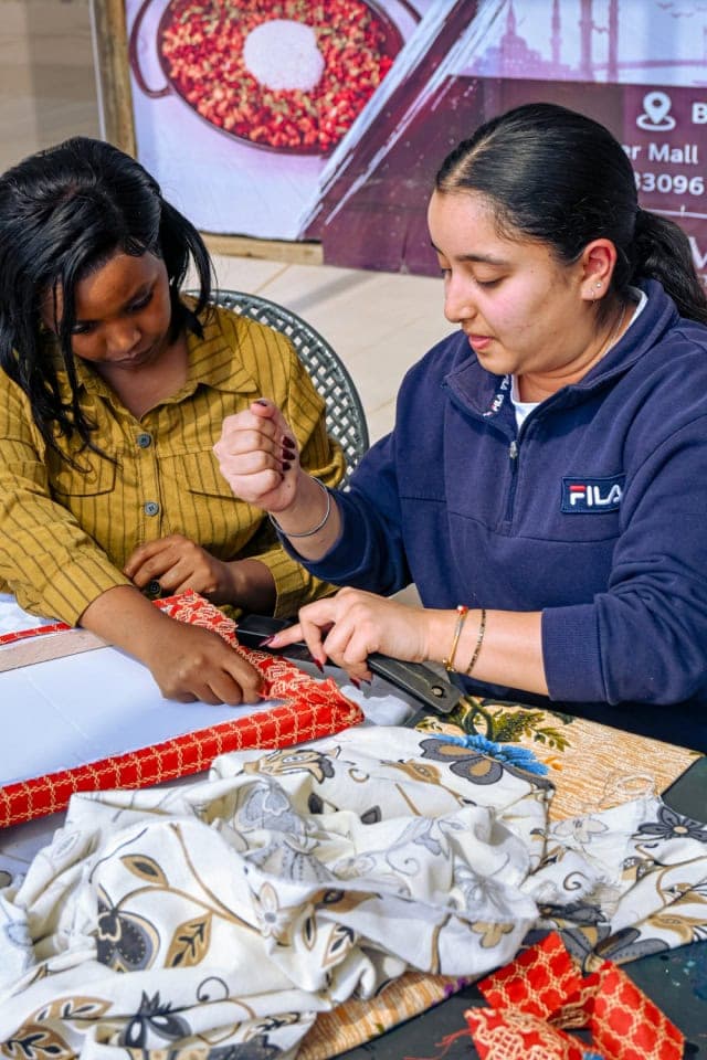 A participant and facilitator stretch patterned fabric around a frame during the Frame and Fabric Workshop.