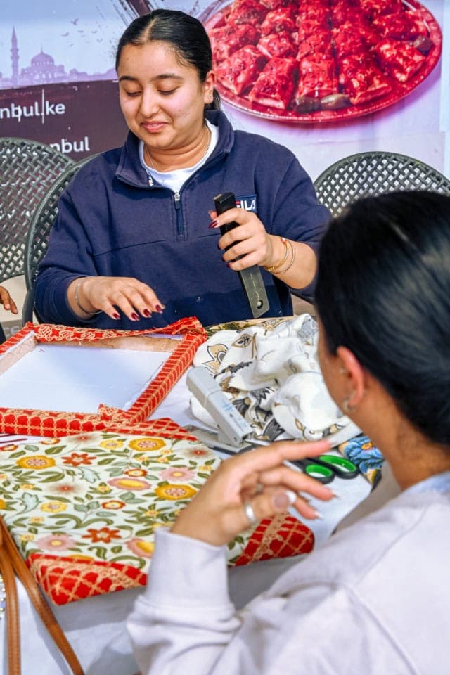 A facilitator demonstrates a crafting tool while a participant follows along at the Frame and Fabric Workshop.