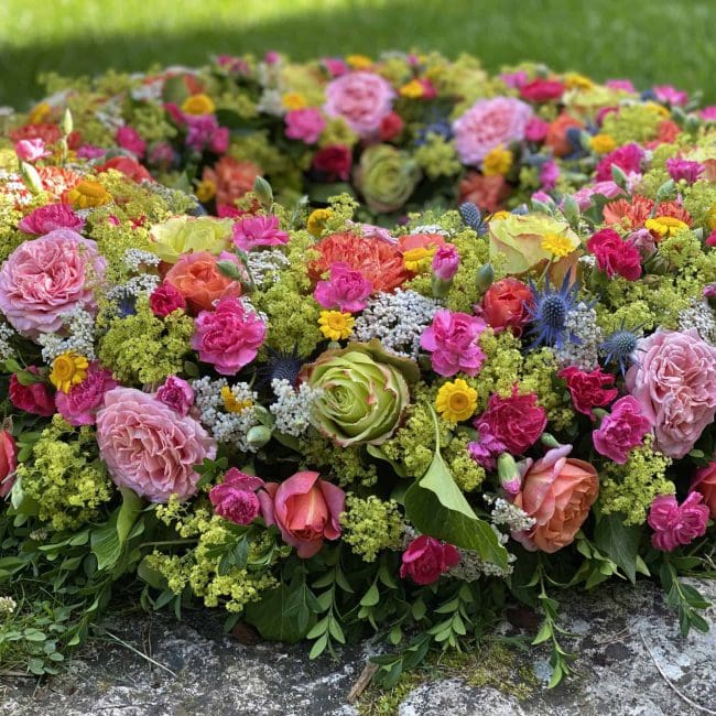 Nahaufnahme Moderner Bunter Trauerkranz ca. 80 cm Durchmesser mit blauen Disteln - Mannstreu, Farbige Freiland Rosen, Frauenmantel, Schafgabe, pinke Nelken, gelbe Färberkamille für Beerdigung in Pfaffenhofen / Ilm