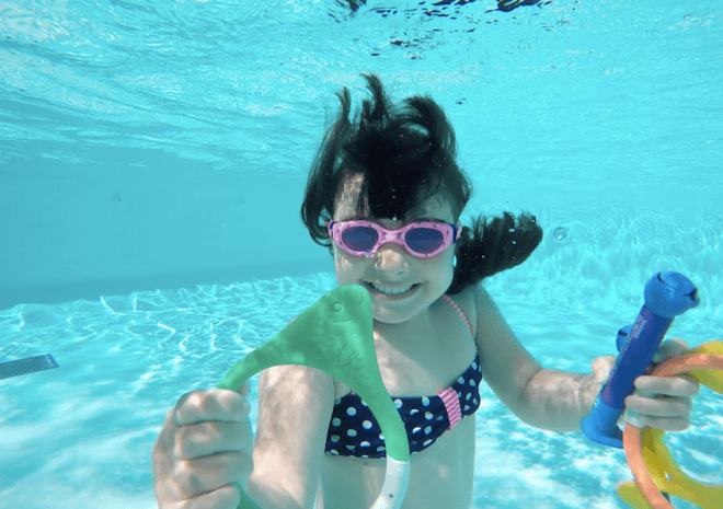 a happy girl swims under the water in summer in an outdoor swim pool
