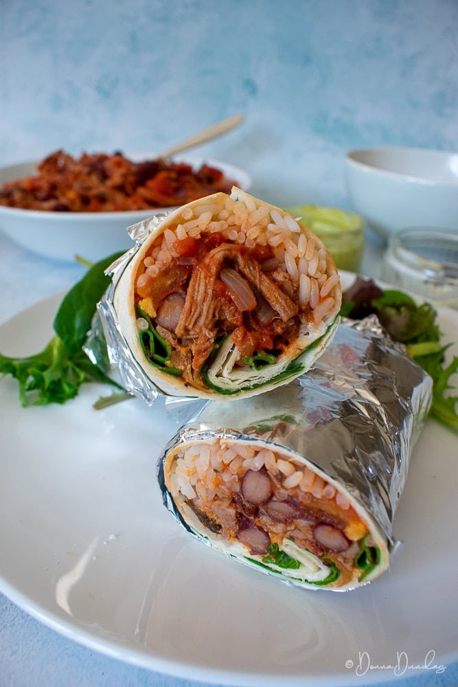 leftover beef burritos, wrapped in foil, cut in half and stacked on plate.