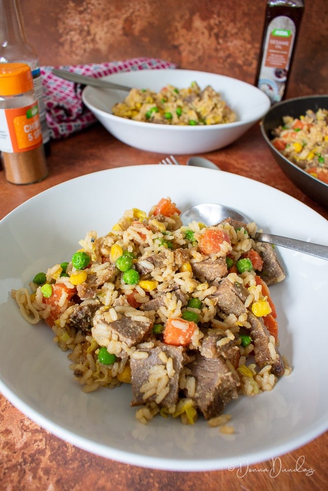 served portion of fried rice in bowl, another bowl, sauces and frying pan in the background.