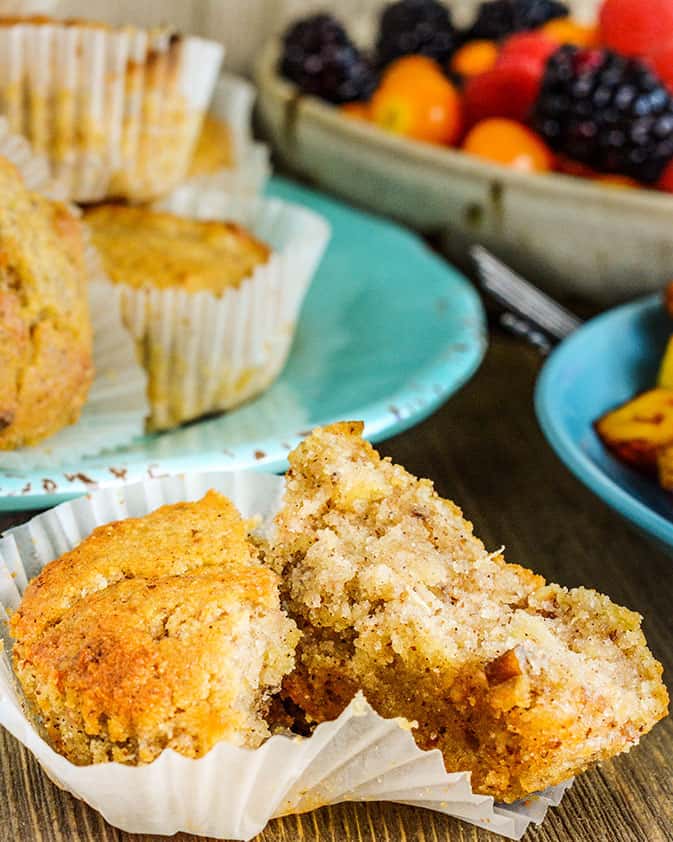 hummingbird muffin broken in half in white wrapper with pile of muffins in the background