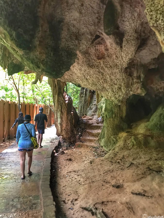 three people walking beside a cave with stalactites near railay beach