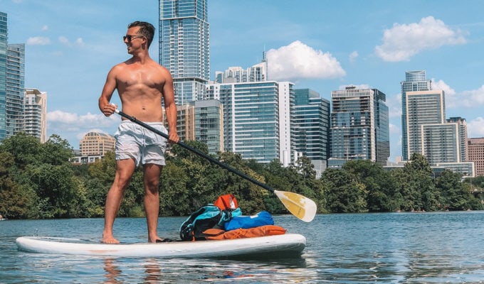 Man standing on inflatable stand up paddle board with bags on the front