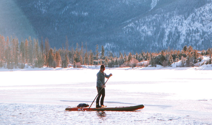 Person stand up paddle boarding on a frozen lake in the mountains