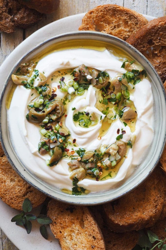 This Garlic Confit Goat Cheese Dip with Spicy Lemony Olives is creamy, tasty and easy to make. Oh! And it's a 3 in one dip: a spreadable garlic confit cheese base, homemade toasts and the most delicious olive topping. It makes a delicious appetiser and it's perfect for any occasion and all year round! | Paula's Apron Recipe