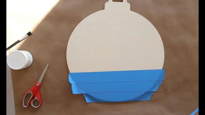 how to paint snow, putting blue painter's tape on the back of wood ornament-shaped blank 